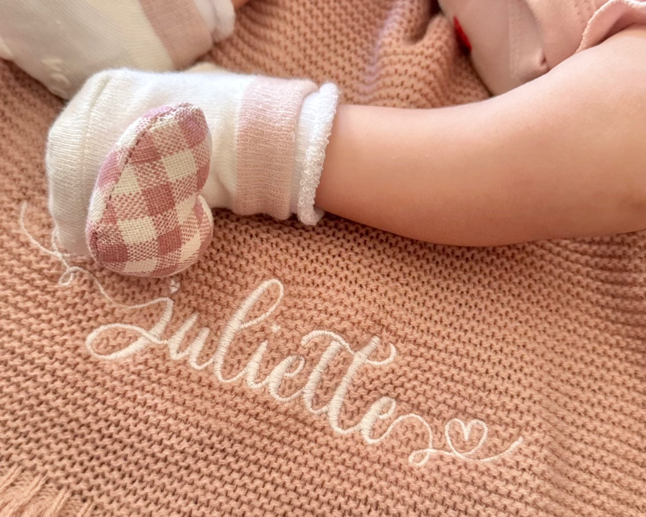 Child's legs in white socks on a beige blanket with 'Juliette' embroidered.