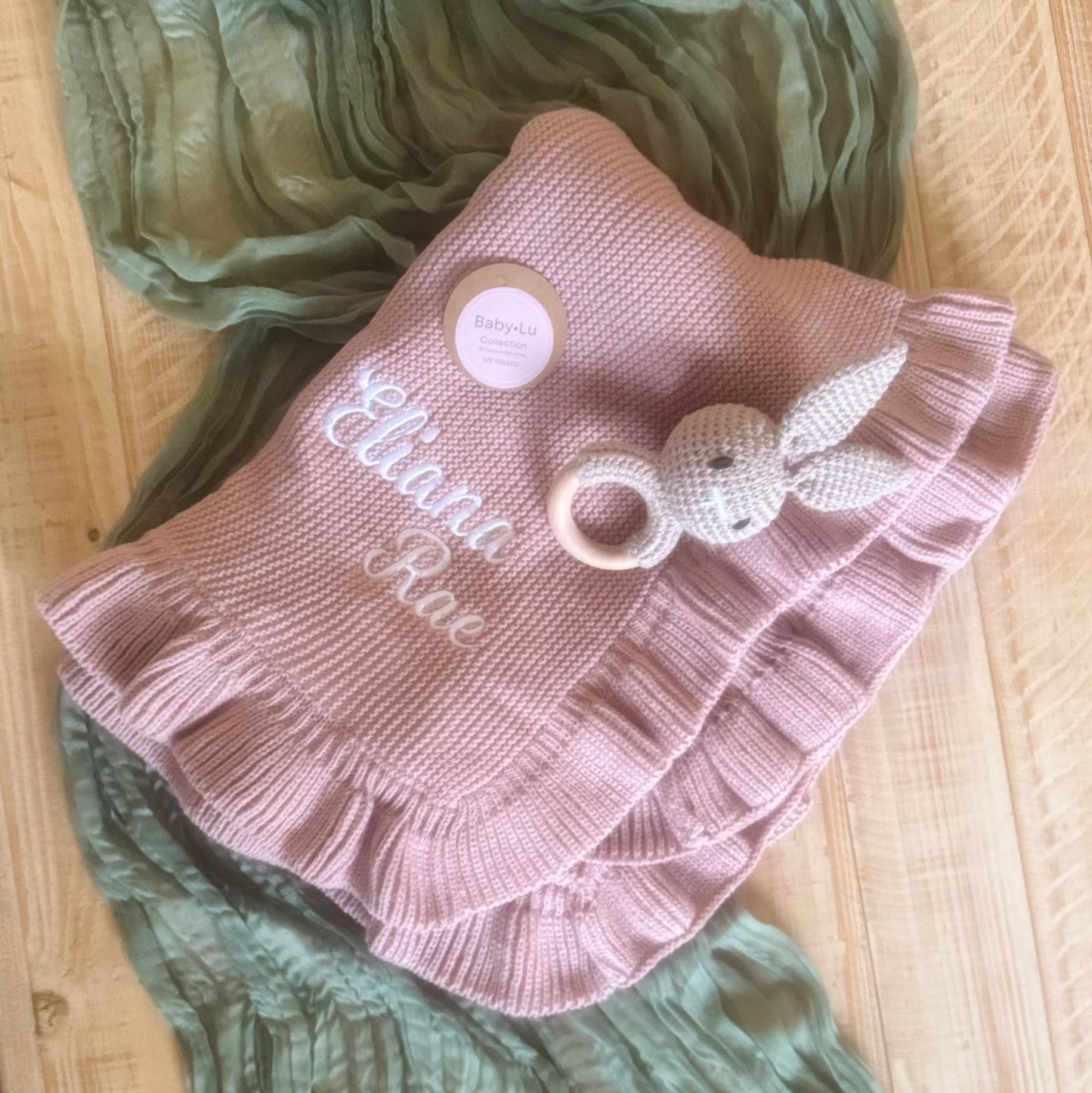 Pink ruffled blanket with embroidered name on a wooden surface